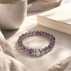 AURA Amulet amethyst crystal bracelet resting in warm sunlight beside a journal for self-care.
