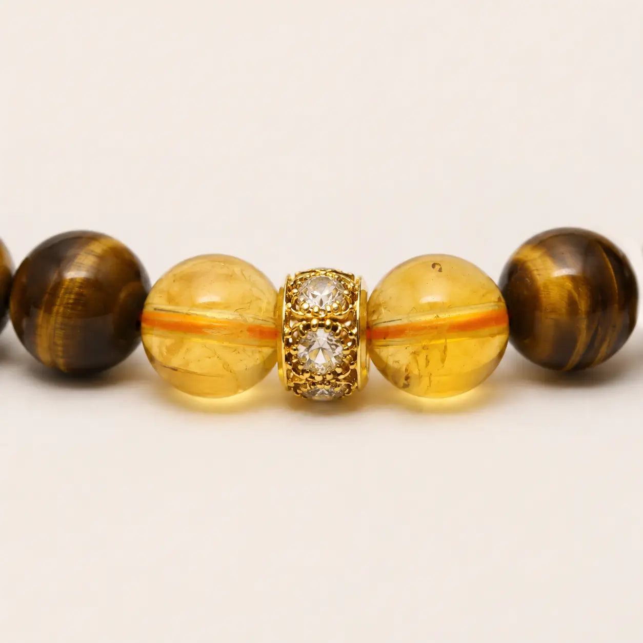 AURA Amulet macro close-up of citrine beads and gold-plated spacer on a tiger eye stone bracelet for wealth.