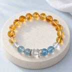 Citrine crystal bracelet with blue aquamarine, clear quartz and silver-tone lotus caps on an ivory stone platform