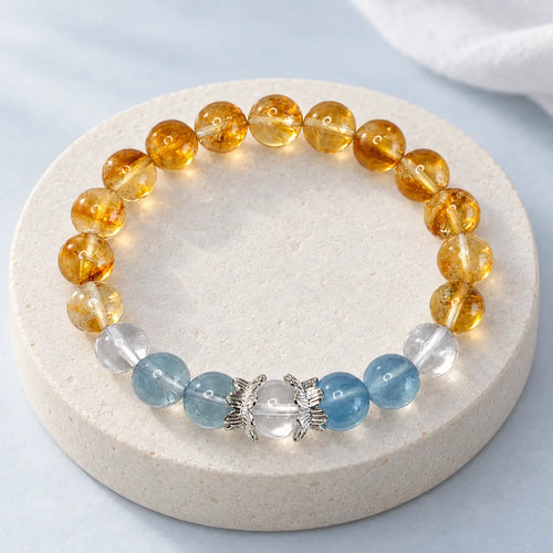 Citrine crystal bracelet with blue aquamarine, clear quartz and silver-tone lotus caps on an ivory stone platform