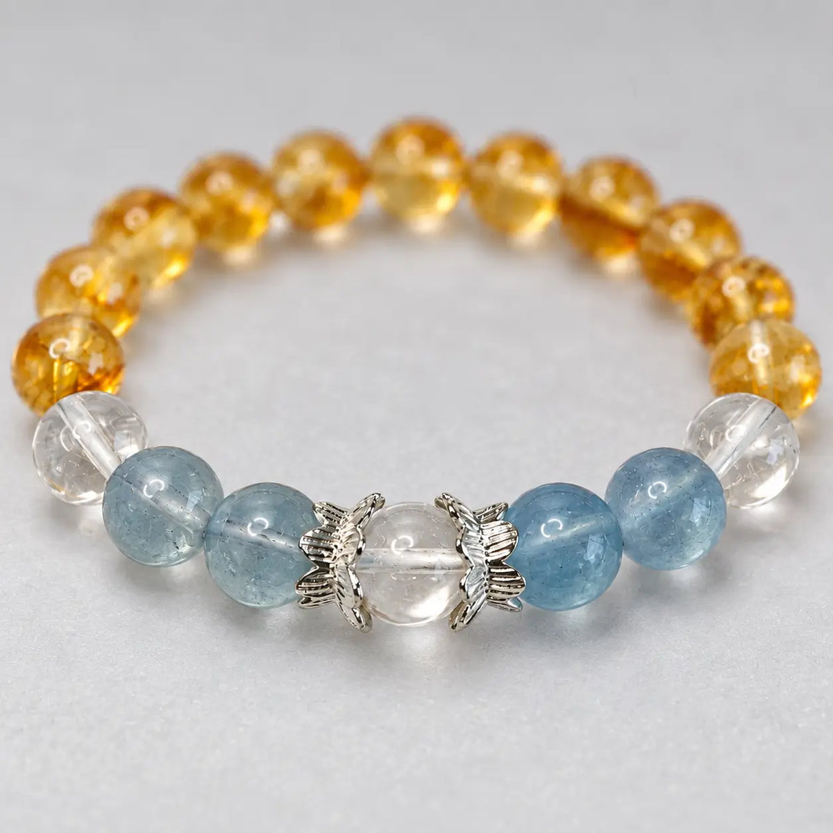 Close-up of a clear quartz center bead between silver-tone lotus caps, with blue aquamarine beads on both sides.
