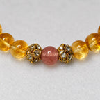 Close-up of a strawberry quartz bead between two gold-tone floral spacers and yellow citrine beads.