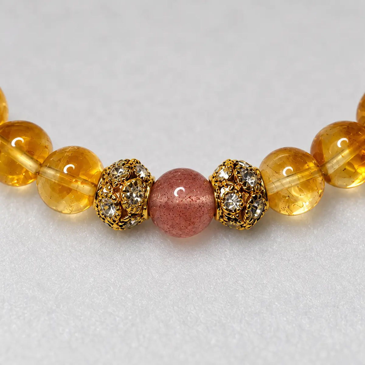 Close-up of a strawberry quartz bead between two gold-tone floral spacers and yellow citrine beads.