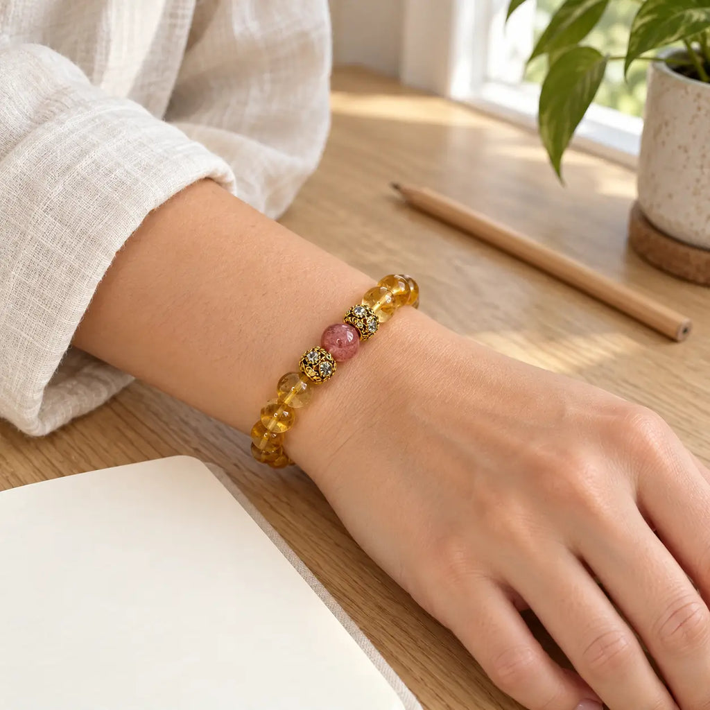Citrine bracelet worn on a wrist, with a strawberry quartz center bead and gold-tone floral spacers.