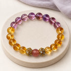 Citrine and amethyst bracelet with a strawberry quartz center bead and gold-tone spacers on a cream stone tray.