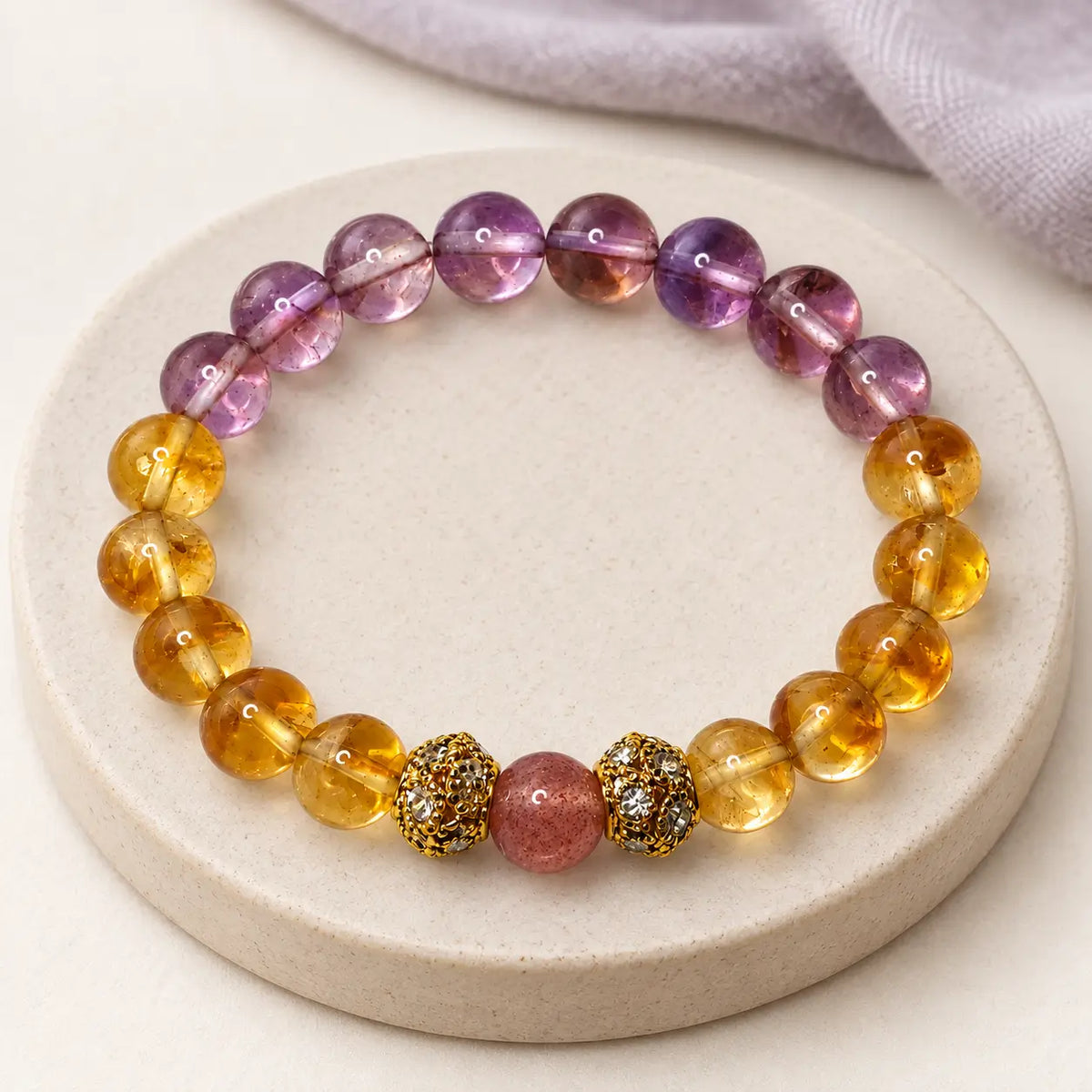 Citrine and amethyst bracelet with a strawberry quartz center bead and gold-tone spacers on a cream stone tray.