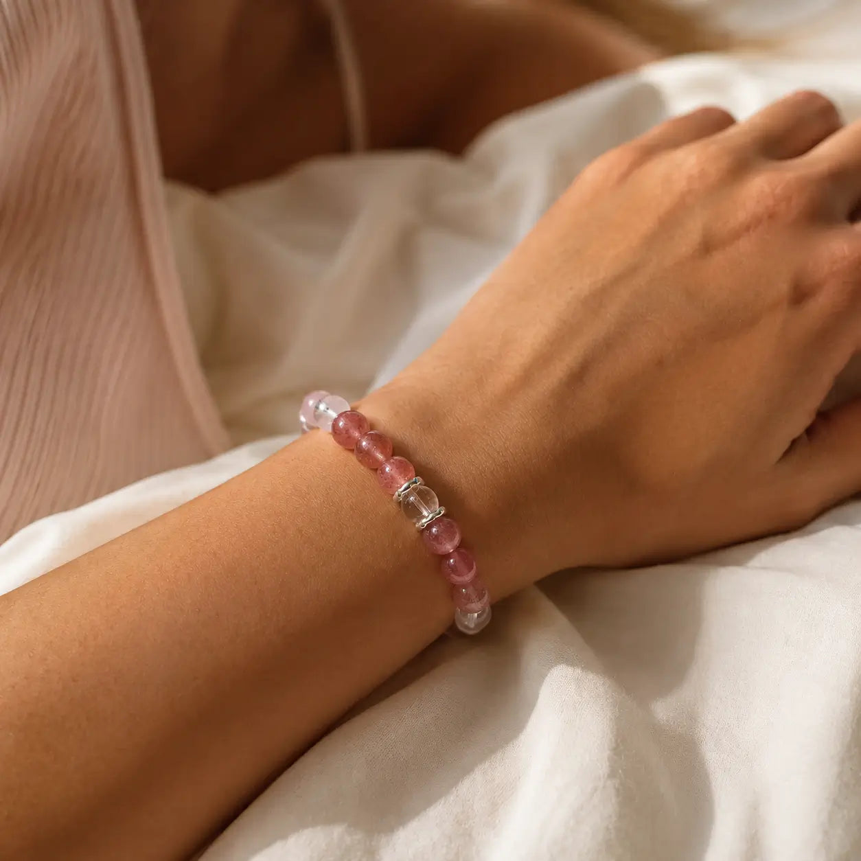 AURA Amulet healing bracelet for women worn on wrist with rose quartz and strawberry crystal in soft sunlight.