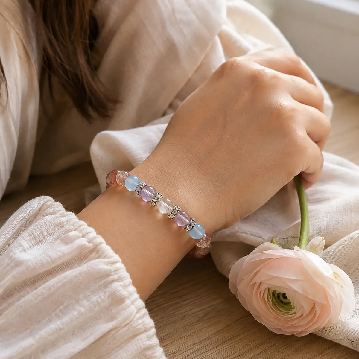Woman wearing the strawberry quartz bracelet beside a pale pink flower in soft natural light