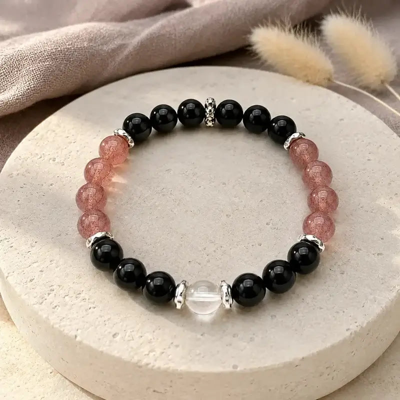 AURA Amulet Obsidian & Strawberry Quartz Spiritual Protection Bracelet on a stone dish, a spiritual bracelet for protection.