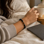 AURA Amulet protective black obsidian bracelet worn by woman holding coffee, a daily energy shield accessory. 