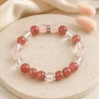 AURA Amulet Strawberry & Rose Quartz Self-Love Bracelet on stone with pink flora, a healing bracelet for women
