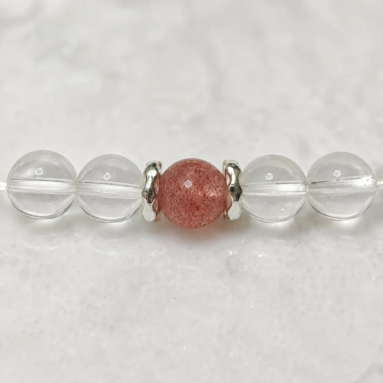 AURA Amulet macro shot of clear crystal quartz and strawberry quartz with silver spacers, a calming anxiety bracelet.